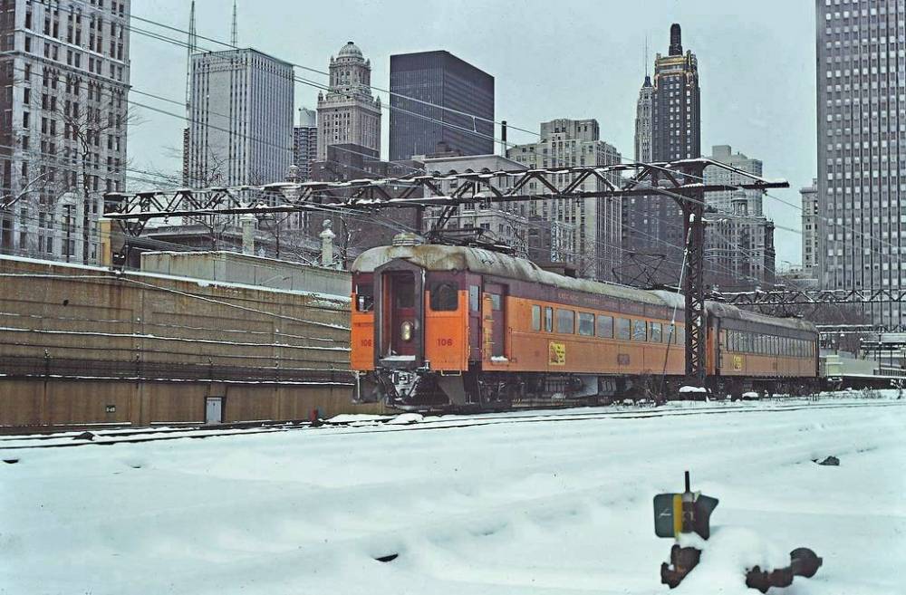A PHOTO - CHICAGO - SOUTH SHORE LINE ELECTRIC COMMUTER TRAIN HEADING S - PART OF SKYLINE BEHIND - 1976
